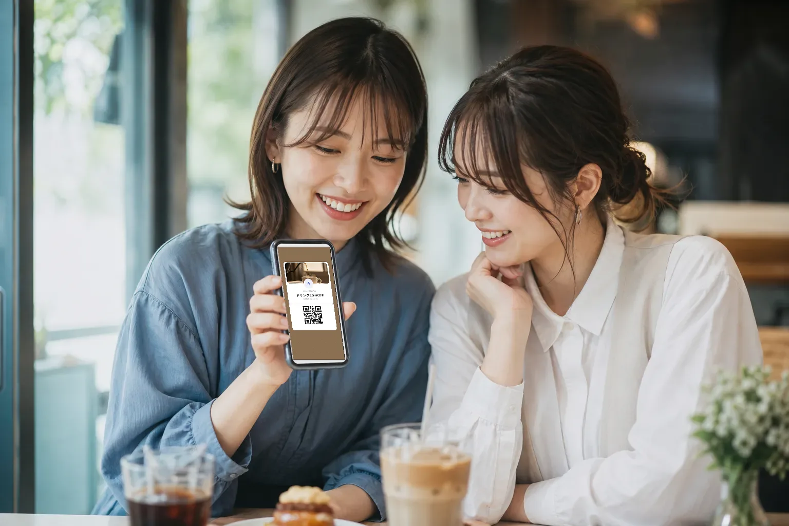 カフェで友人とスマホを見て笑い合うシーン